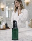Woman applying skincare product in front of a mirror with a bottle of 'Vibrant' on the counter.