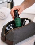 Person reaching into a gray toiletry bag with grooming products on a marble surface.