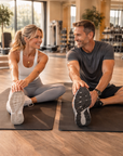 Man and woman stretching together on exercise mats in a gym.