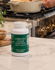 Supplement bottle labeled 'Vibrant Crave Control' on a kitchen counter with cooking activity in the background.