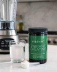 Vibrant Creatine supplement container on a kitchen counter with a blender and glass of liquid in the background.
