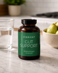 Vibrant Gut Support supplement bottle on a kitchen counter with a glass of water and pears.