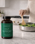 Bottle of 'Vibrant Gut Support' on a kitchen counter with a person cooking.