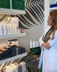 Woman in a white coat standing in a store with skincare products on shelves.