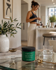 Woman in a kitchen with a jar of 'Vibrant Boost' on a table.