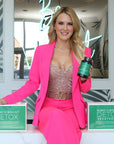 Woman in a bright pink outfit holding a bottle of '14 Day Vibrant Detox' in a stylish interior setting.