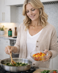 Woman cooking in a kitchen, holding a bowl of vegetables and stirring a pan.