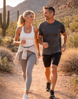 Man and woman jogging together in a desert landscape with cacti and mountains.