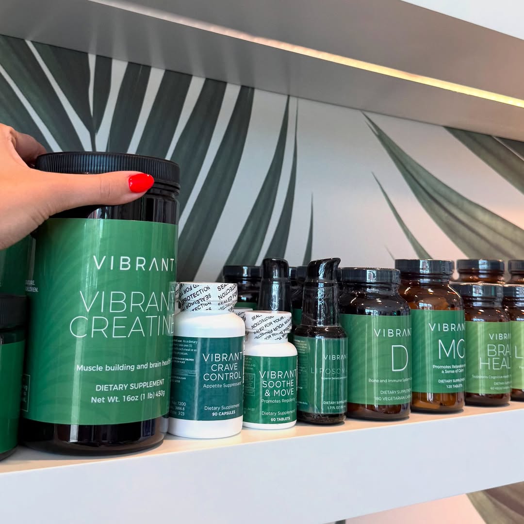 Hand holding a 'Vibrant' supplement bottle with various other supplements on a shelf.