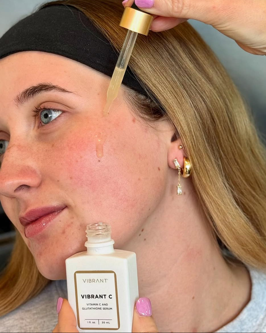 Person applying a dropper of a product to their face with a bottle labeled 'Vibrant C' in the foreground.